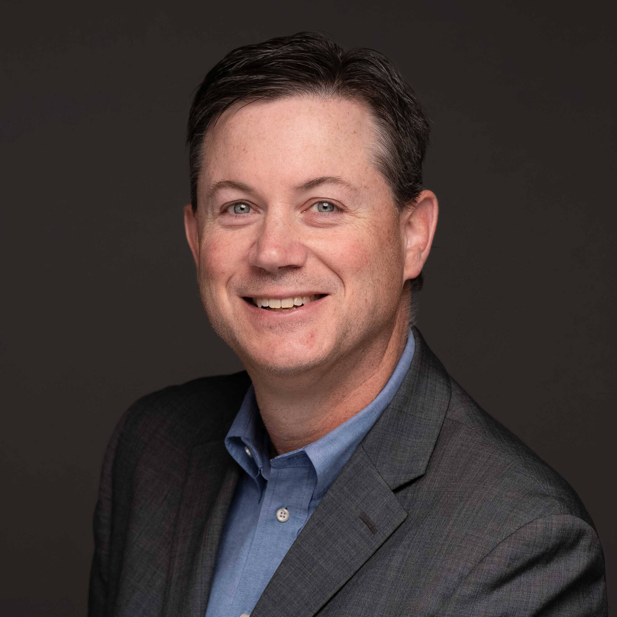 Bill Herbst wearing a gray suit jacket and a blue button-up shirt